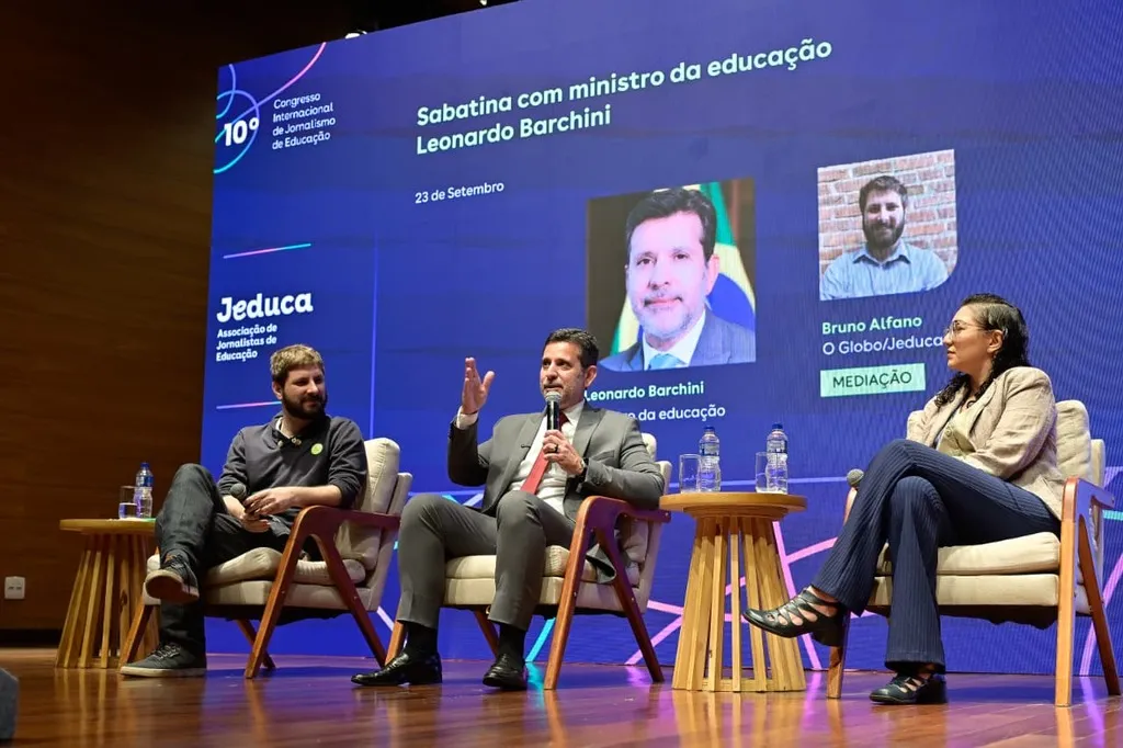 Imagem mostra dois homens e uma mulher, sentados. Ao fundo, um painel de led com informações sobre o evento